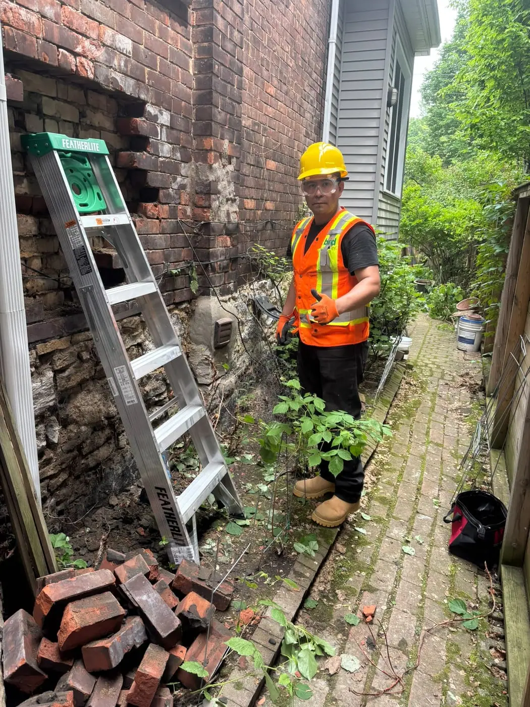 Contractor beside a brick wall opening in a narrow passage, with salvaged bricks stacked below