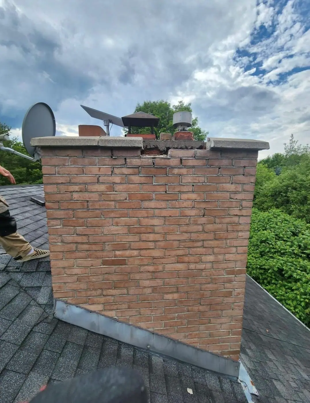 Brick chimney stack with a stone cap on a shingled roof