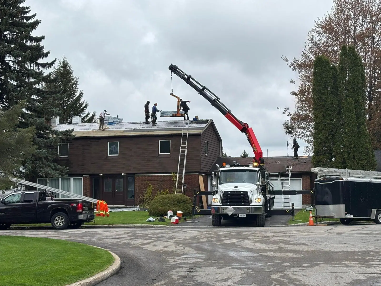 Crane lifting materials to workers on a roof beside a house