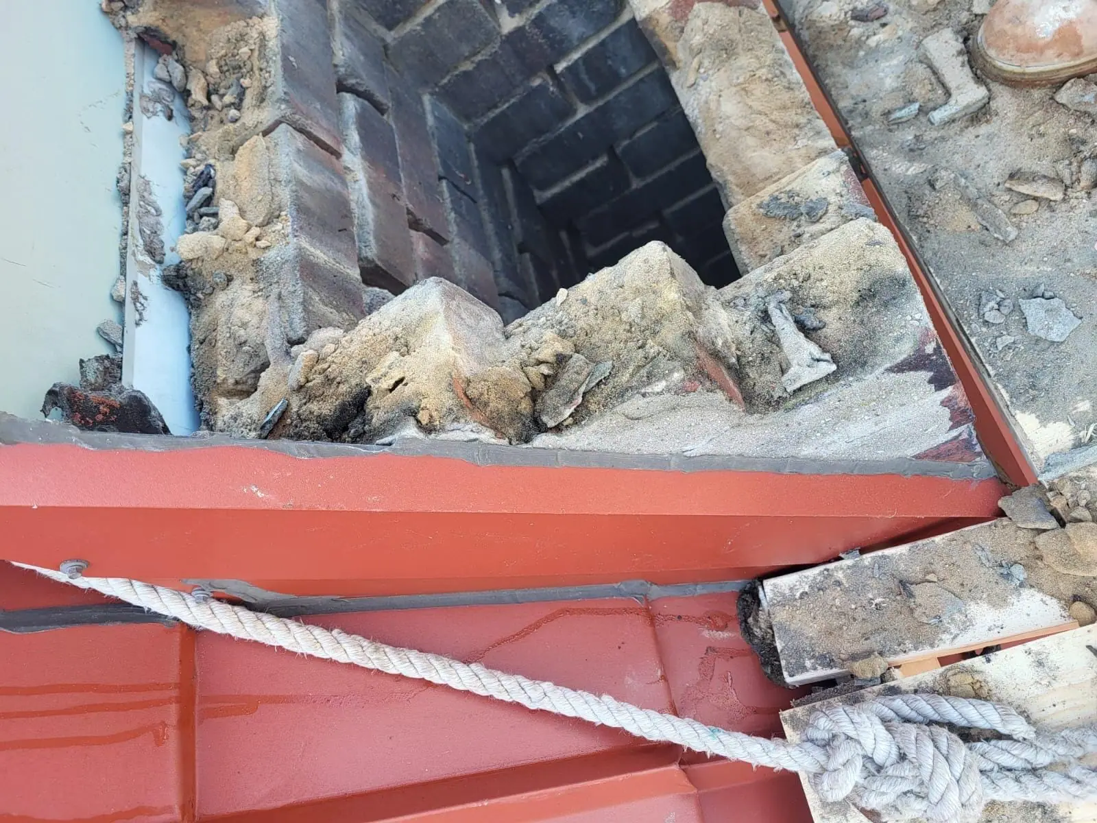 Novastone Contracting work in progress: flue opening with loose masonry and a rope on a metal roof