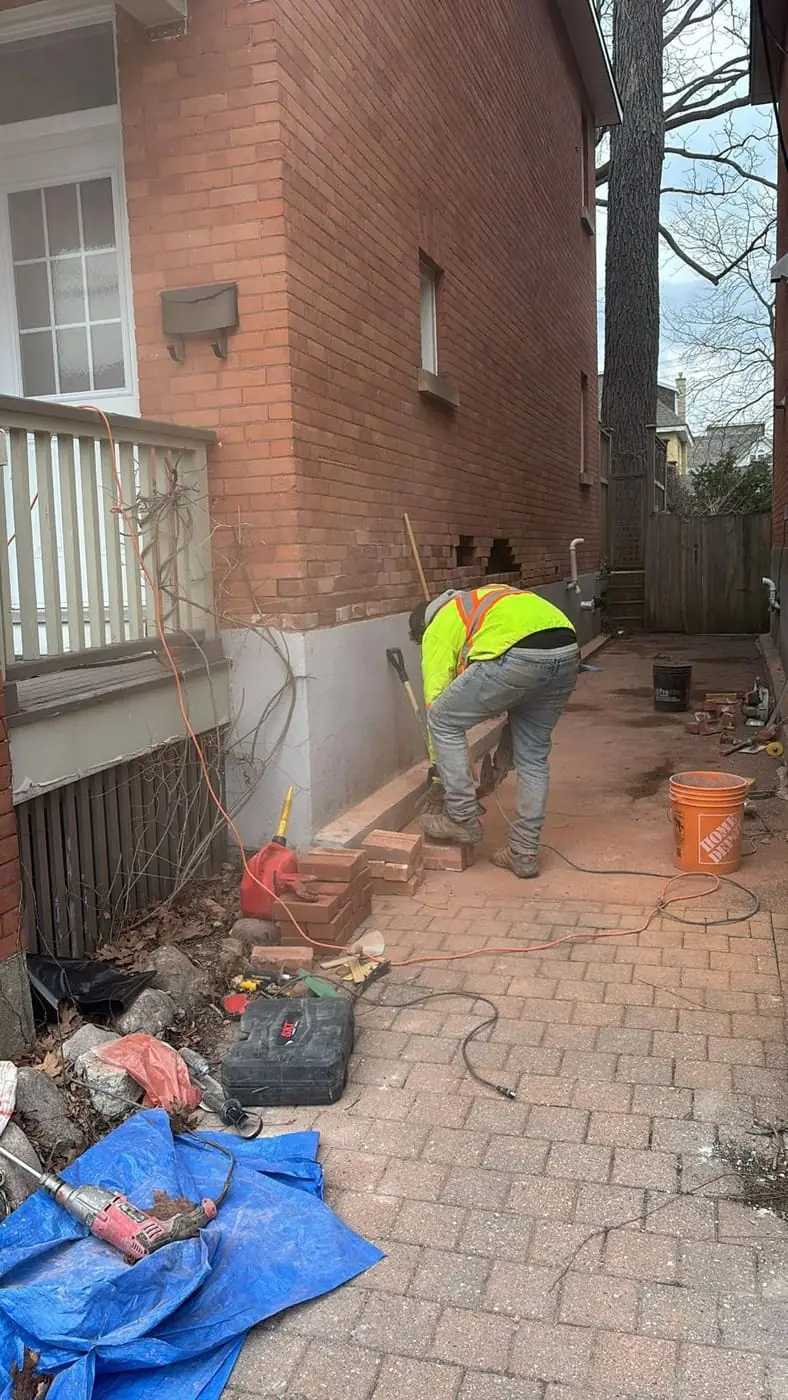 Novastone Contracting crew member carrying out demolition at the base of a brick house