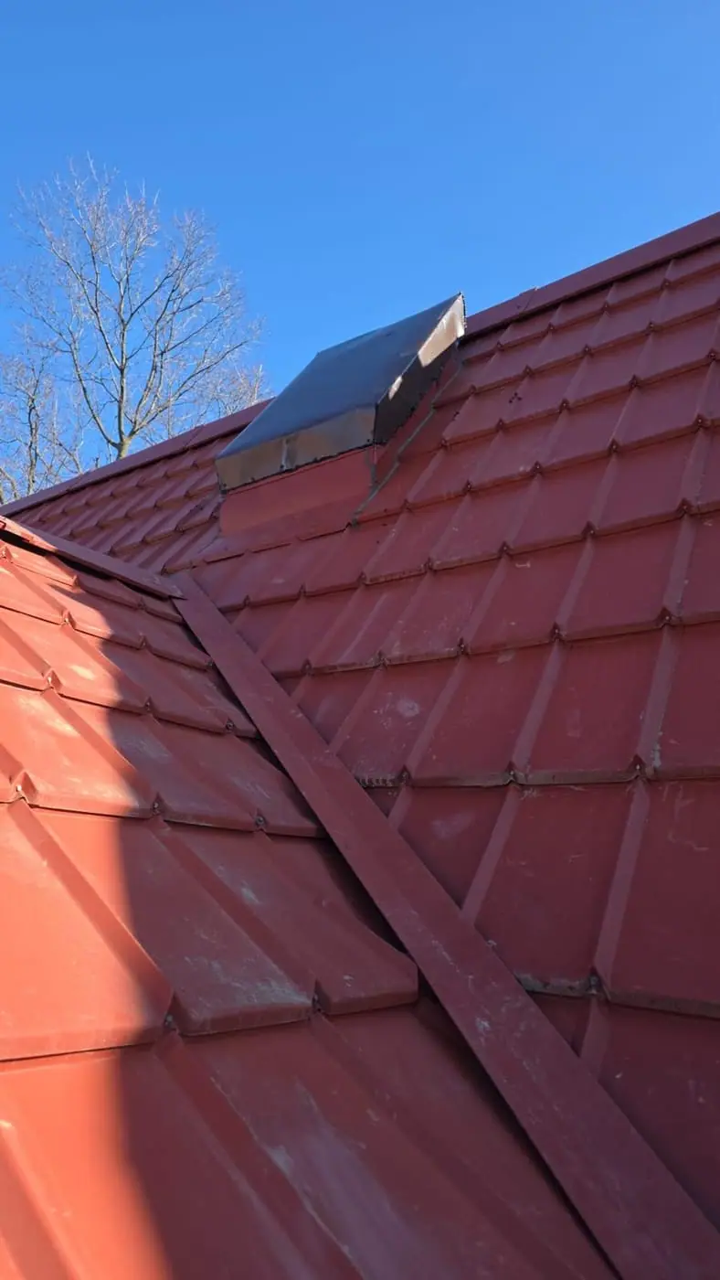 Red metal roof with a valley flashing and a chimney in the distance