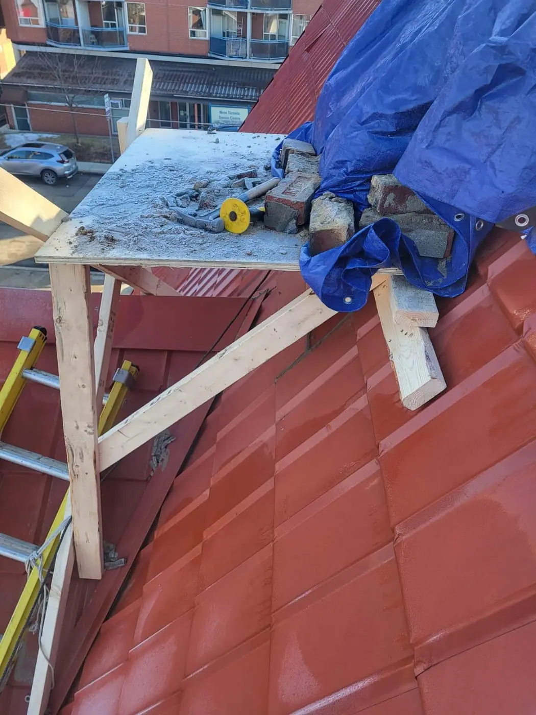 Timber work platform with tools, bricks and a tarp on a metal roof