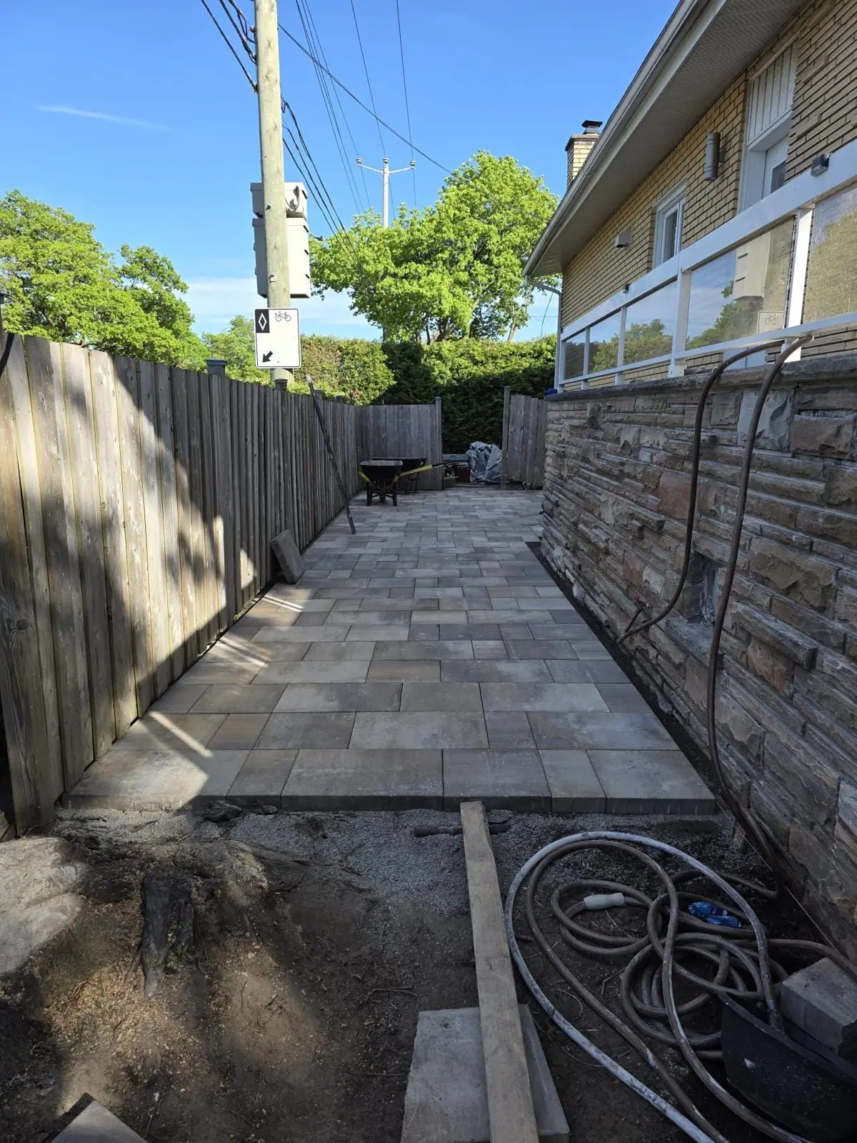 The same side yard after paving: finished interlocking pavers beside the stone-clad wall