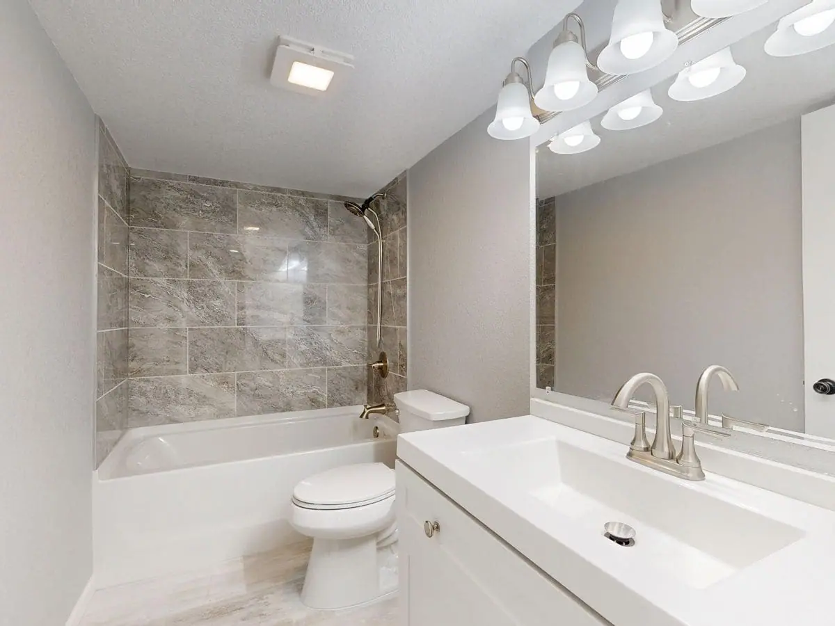 Renovated bathroom with tiled tub surround, vanity and mirror