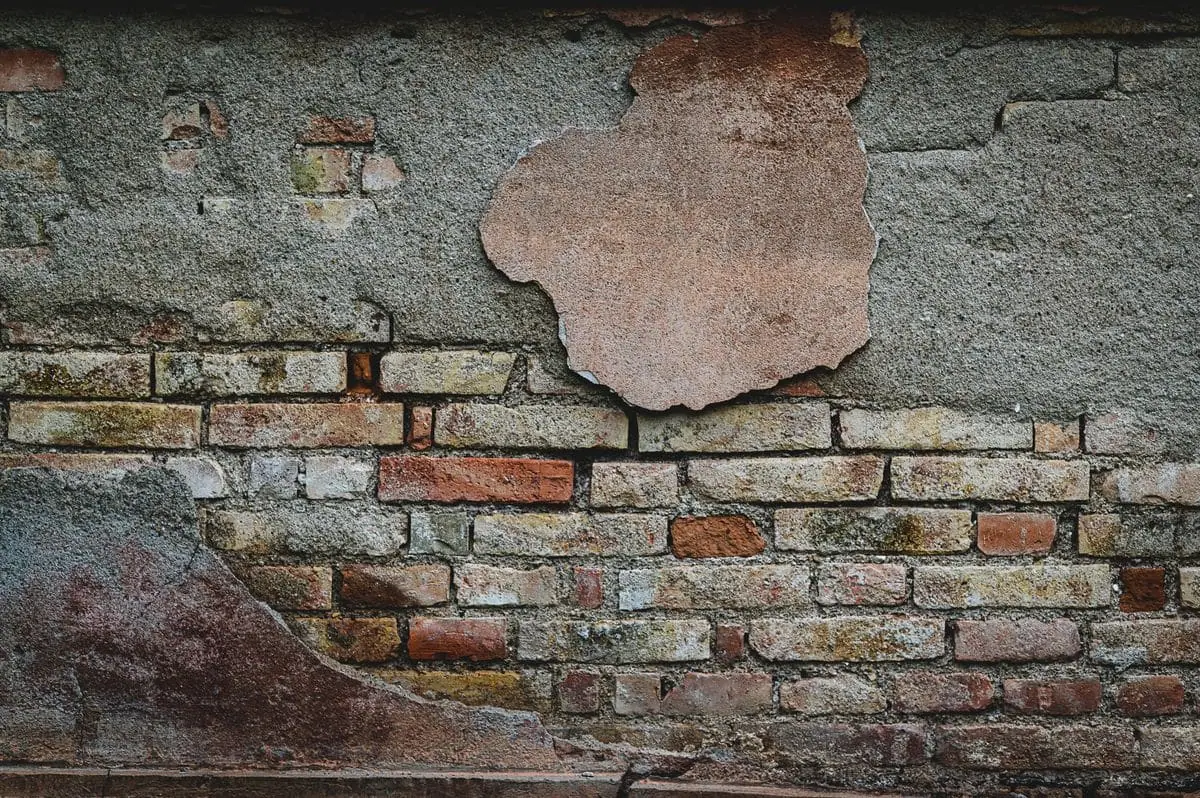 Old brick wall with crumbling plaster and eroded mortar joints