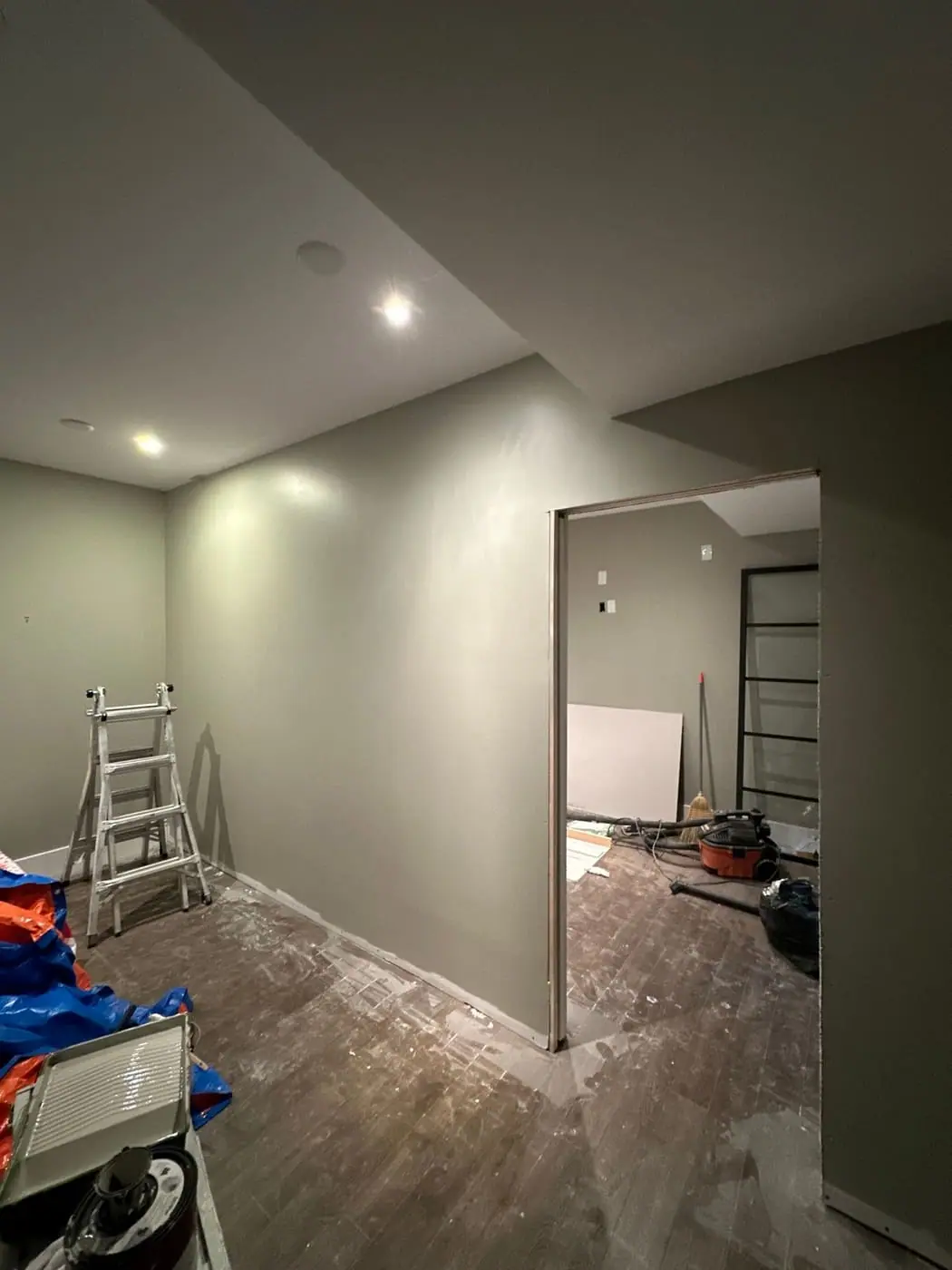 Basement-style room mid-renovation with fresh drywall, a stepladder and tools